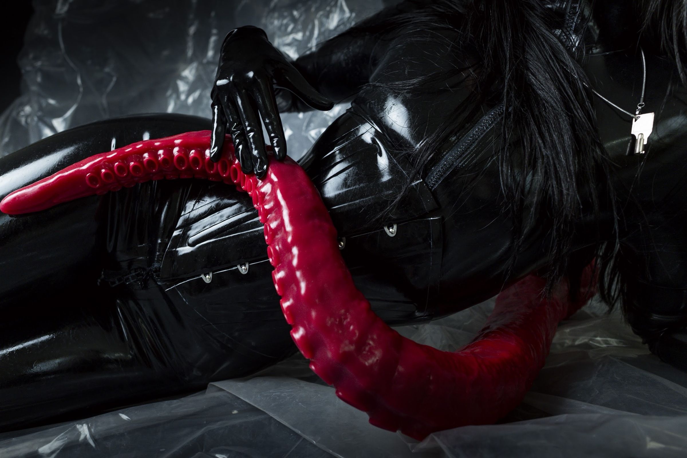 Black latex, a gloved hand on a red tentacle, a key at her throat
